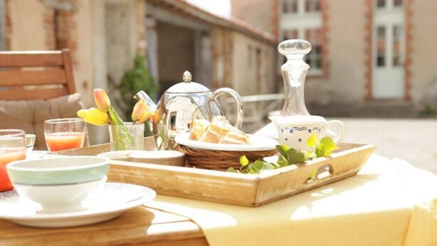 A breakfast setup with a tray of bread, a jug, and a teapot on a wooden table.