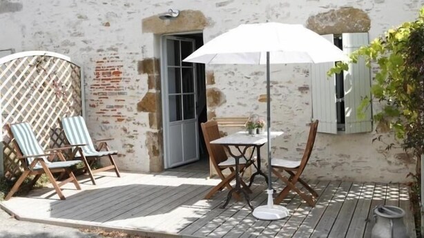 A patio with a table and chairs, a white umbrella, and a wooden deck.
