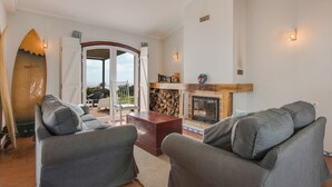 Una sala de estar con sofás grises, una mesa de centro de madera, una chimenea y una tabla de surf en la pared.