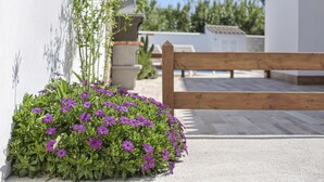 A wooden bench, a concrete pathway, and a flower bed with purple flowers. - Vacation Home "Rocamar" with Mountain View, Pool, Wi-Fi, A/C, Terrace & Garden (Barbate)