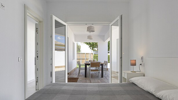 A bedroom with a large bed, a bedside table with a lamp, and a view of an outdoor patio with a table and chairs. - Vacation Home "Rocamar" with Mountain View, Pool, Wi-Fi, A/C, Terrace & Garden (Barbate)