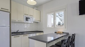 A modern kitchen with white cabinets, a built-in microwave, and a large island with chairs. - Vacation Home "Rocamar" with Mountain View, Pool, Wi-Fi, A/C, Terrace & Garden (Barbate)