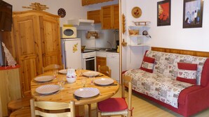 Una cocina acogedora con armarios de madera, una mesa de comedor preparada para cuatro personas y un sofá rojo con cojines estampados.