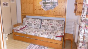 Una habitación acogedora con un sofá cama de madera, una mesita pequeña de madera y un muro con un recorte decorativo.