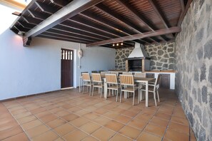 Un patio al aire libre con muro de piedra, una parrilla y una mesa con sillas.
