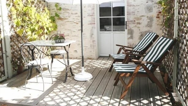 Eine Holzterrasse mit Tisch, Stühlen und einem weißen Sonnenschirm, sowie eine Tür, die zu einem Raum führt.