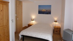 A bedroom with a bed, wooden wardrobe, two bedside tables with lamps, a painting on the wall, and a television on a wooden stand. - Chalet for 8 pers. with large terrace and parking (Les Contamines-Montjoie)