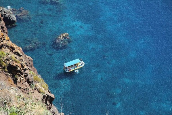 A boat on clear blue water near rocky terrain.
