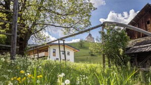 Un paisaje rural con una casa, una estructura de madera y una colina con un edificio al fondo.