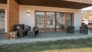 Un edificio moderno con un patio cubierto, mobiliario de mimbre y vistas a un paisaje montañoso.