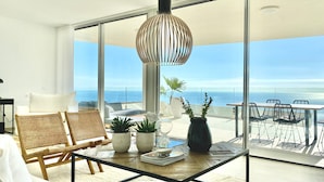 Een modern balkon met een glazen deur, rieten stoelen, een tafel met planten en een hanglamp.