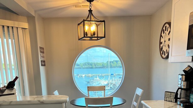 A modern kitchen with a round dining table, white chairs, a built-in oven, and a view of a marina through a large window. - Waterfront Marina View Condo - Walk to Jet Express & Downtown Port Clinton (Port Clinton)