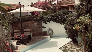 A patio area with a stone wall, a white wall with a hose, and a tiled roof. - Petrino1880 Sea-vacation Apartment in Chalkidiki (Sithonia)