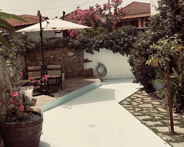 A patio area with a stone wall, a white wall with a hose, and a tiled roof.