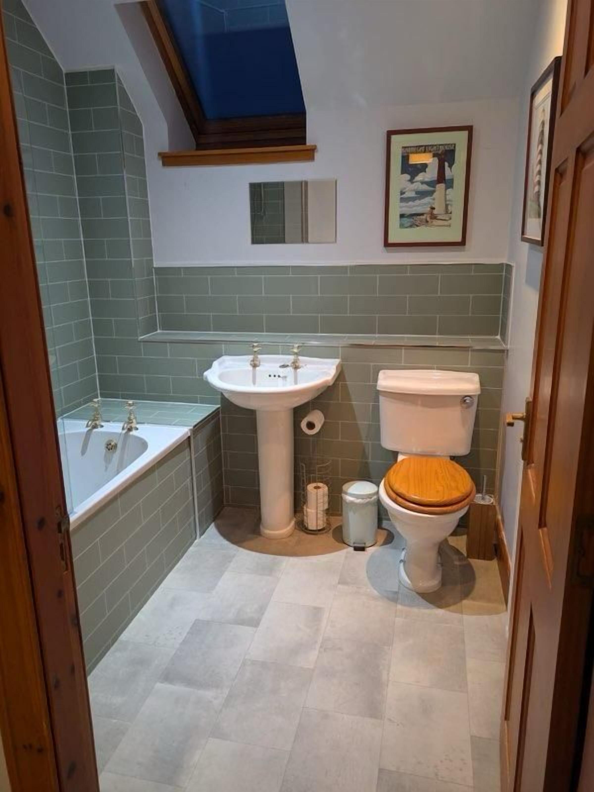 A bathroom with a bathtub, sink, toilet, and a skylight.
