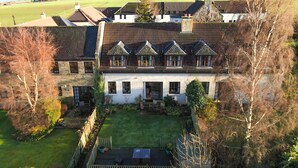 A large, two-story house with a steeply pitched roof, multiple windows, and a well-maintained garden. - Osborne Steading (St. Andrews)