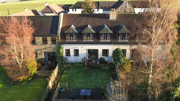 A large, two-story house with a steeply pitched roof, multiple windows, and a well-maintained garden. - Osborne Steading (St. Andrews)
