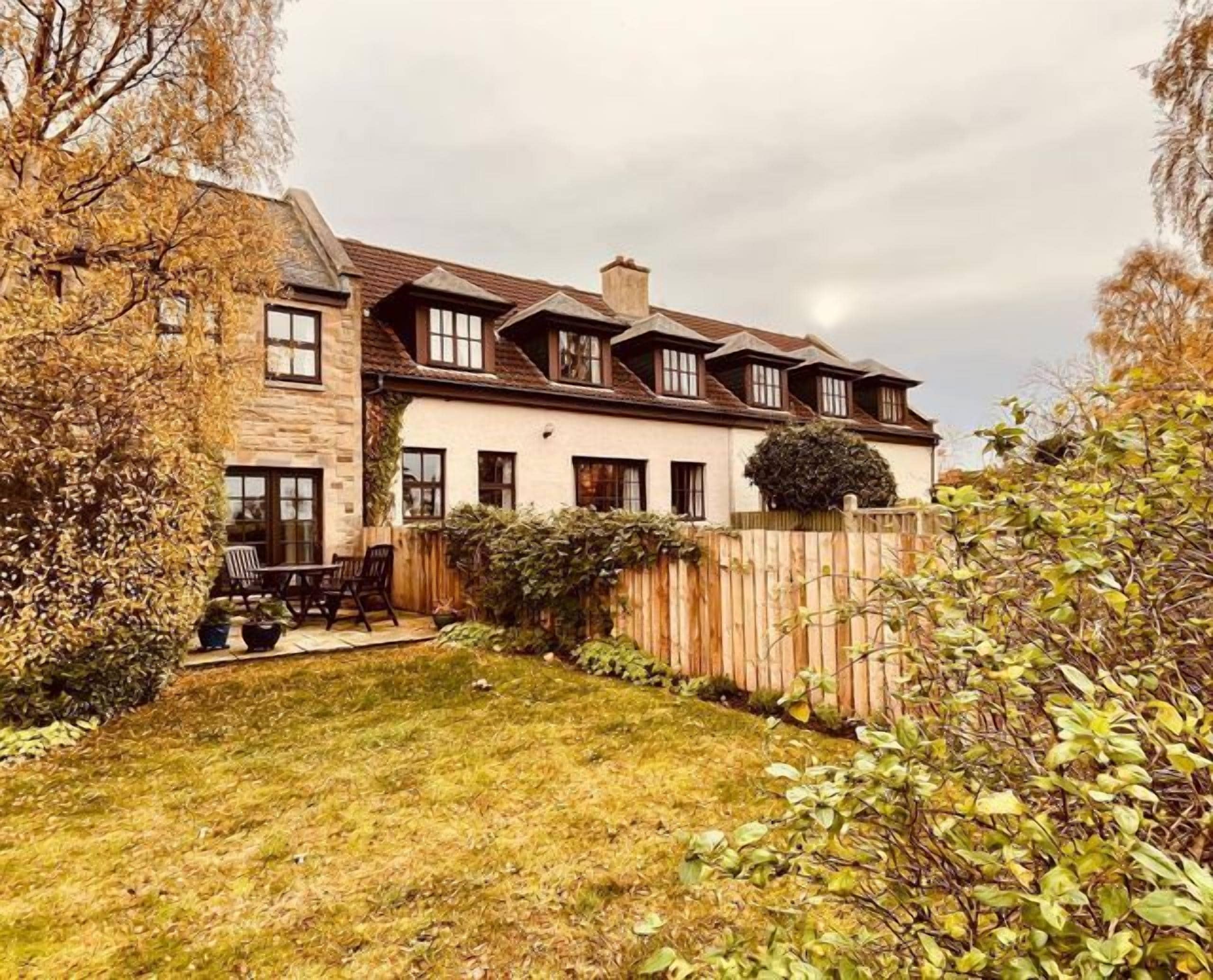 A two-story house with a stone facade, a wooden fence, and a well-maintained lawn.