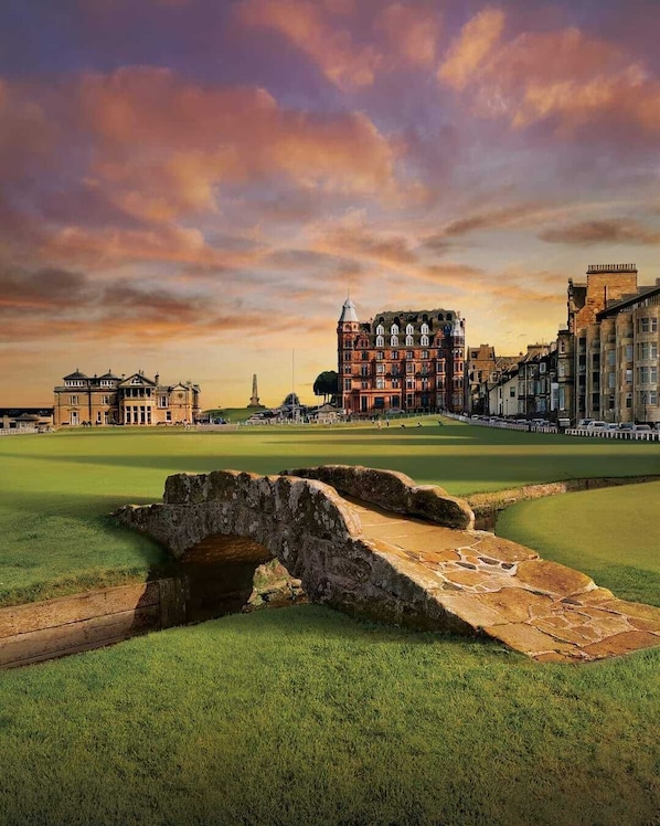 A golf course with a historic building and a stone bridge. - Osborne Steading (St. Andrews)