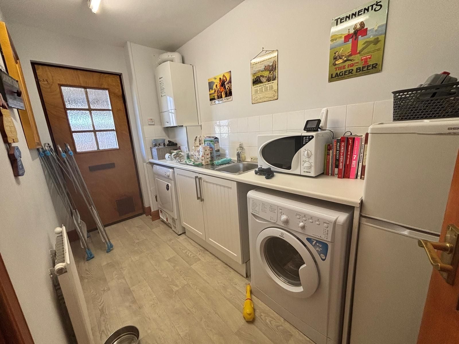 A kitchen with a washing machine, microwave, and a sink. There are books on the counter and a poster on the wall.