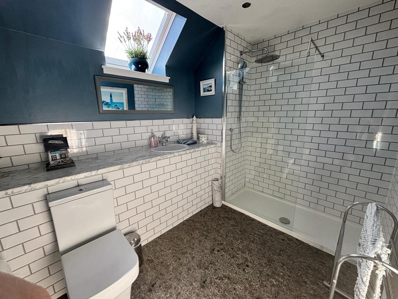A bathroom with white brick walls, a shower, a sink with a marble countertop, and a toilet.