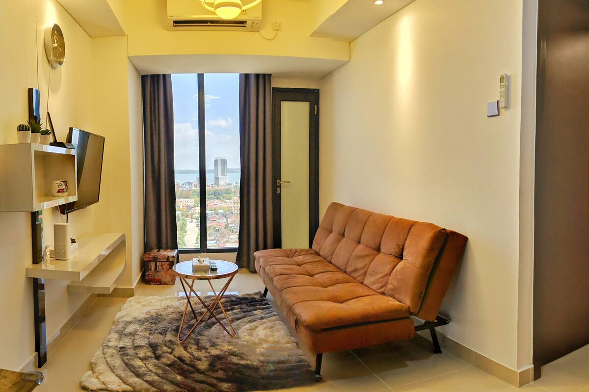 Un salon moderne avec un canapé, une petite table ronde et une grande fenêtre avec des rideaux.