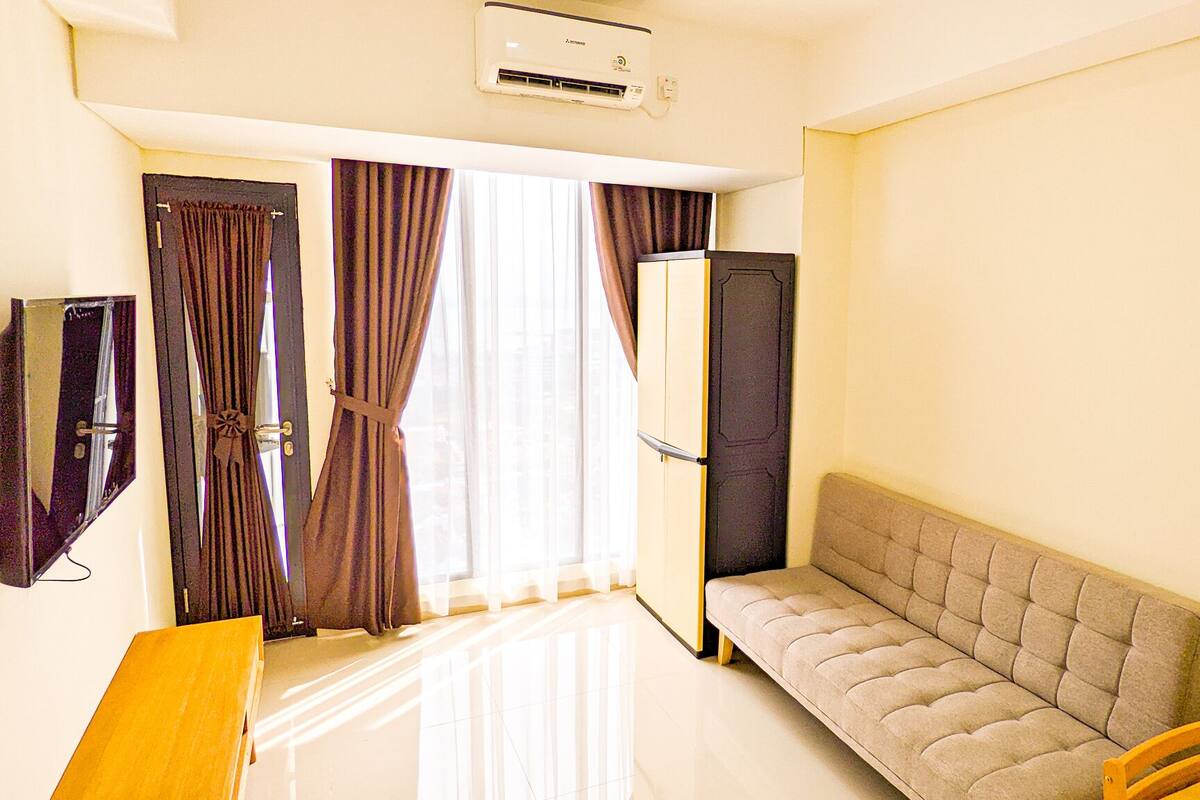 Une chambre d’hôtel de taille réduite, comprenant un canapé, une petite table, un miroir et une armoire.