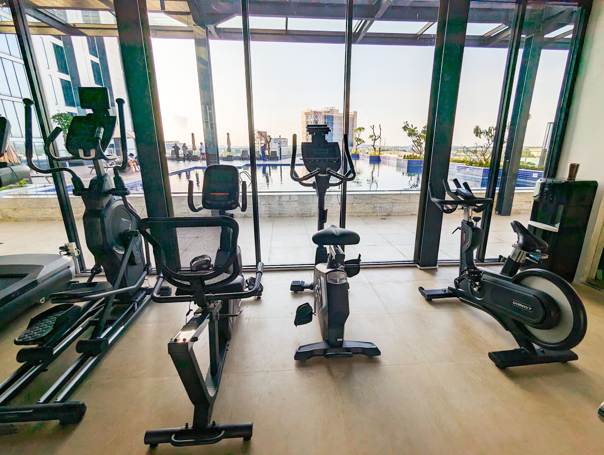 Une salle de sport équipée de divers appareils d’exercice, notamment des tapis de course, des vélos d’appartement et des rameurs, et dotée de grandes fenêtres offrant une vue sur l’extérieur.