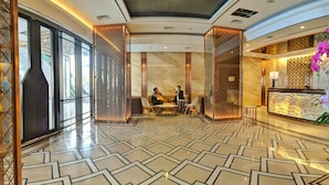 A spacious lobby with a geometric tile floor, a reception desk with a decorative screen, and a seating area with two people conversing. - Lovina at Pollux Meisterstadt (Batam)