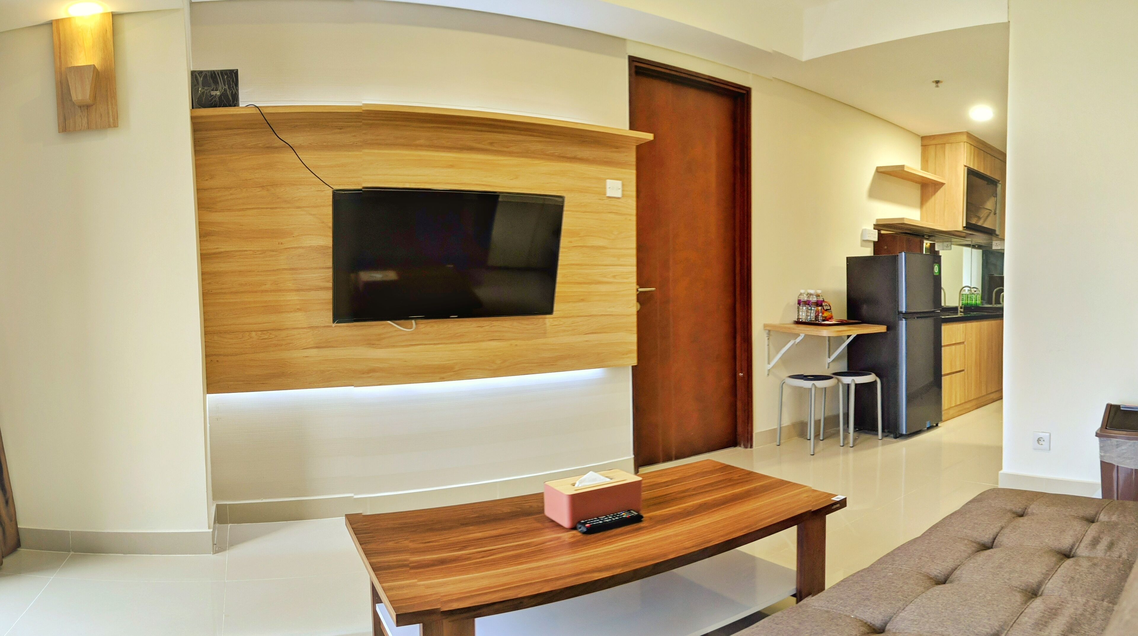 A modern living room with a flat-screen TV mounted on a wooden wall, a wooden coffee table with a remote control, and a cushioned bench.