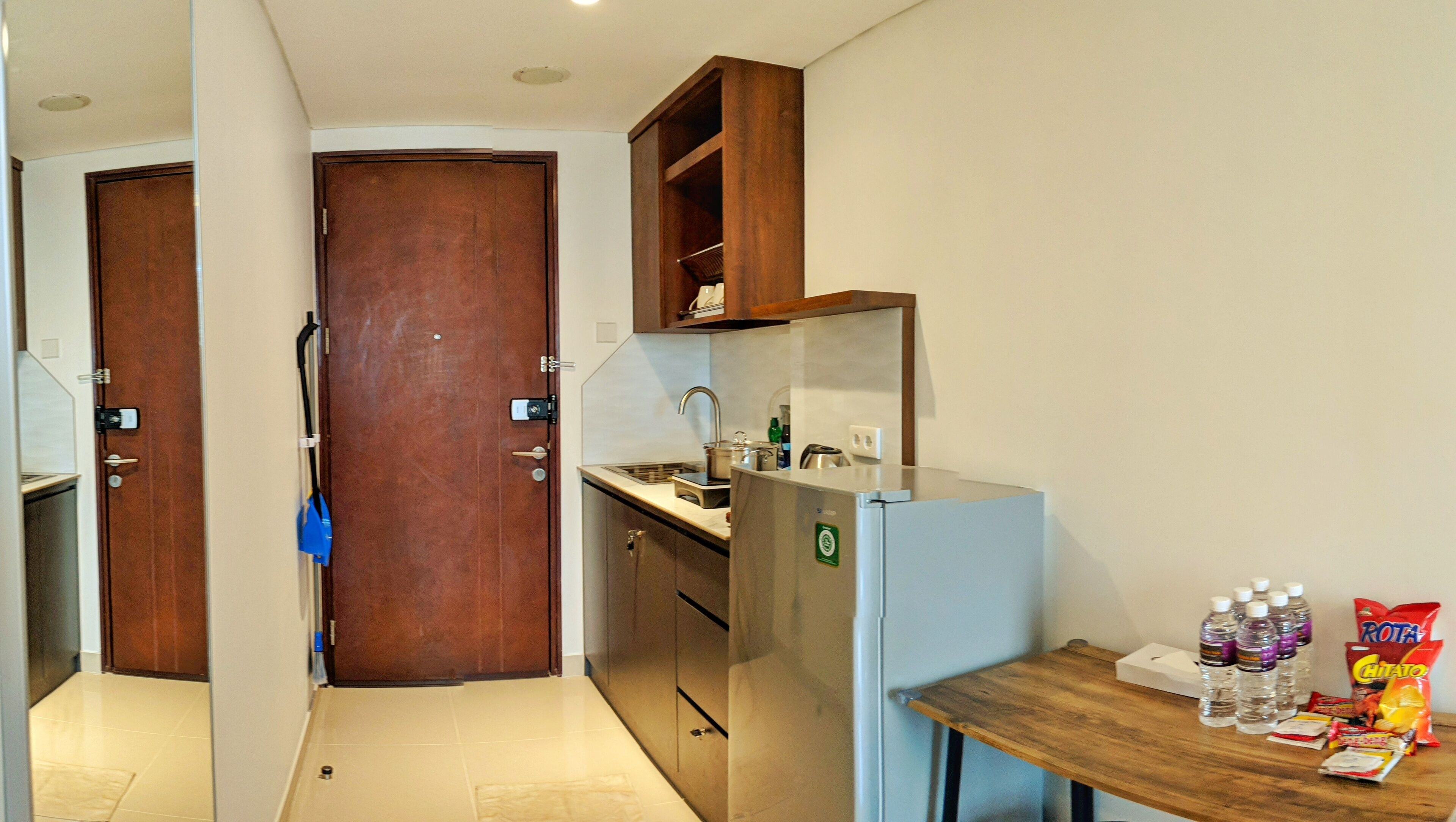 A compact kitchen with a refrigerator, sink, and wooden cabinets. There is a small table with bottled water and snacks.