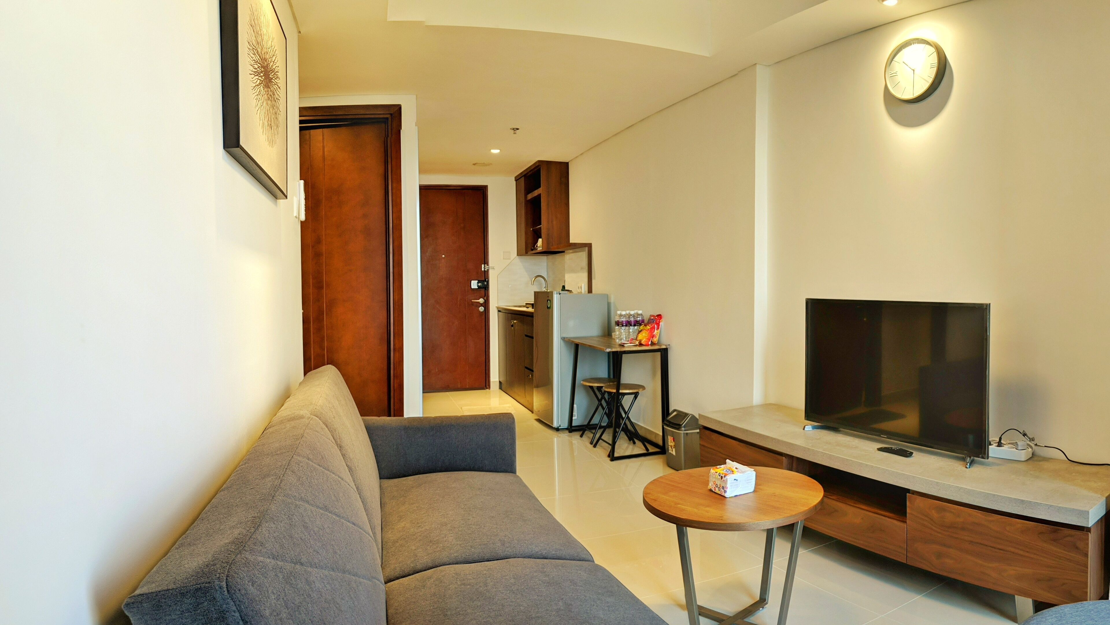 Una sala de estar moderna con un sofá gris, un televisor sobre un mueble de madera y una pequeña mesa redonda con una caja encima.