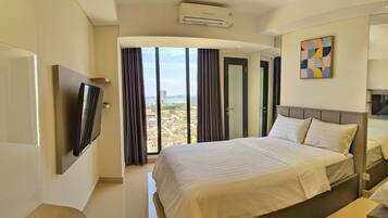 Habitación de hotel con una cama grande, un televisor de pantalla plana en la pared, vistas de la ciudad a través de la ventana y un equipo de aire acondicionado en el techo.
