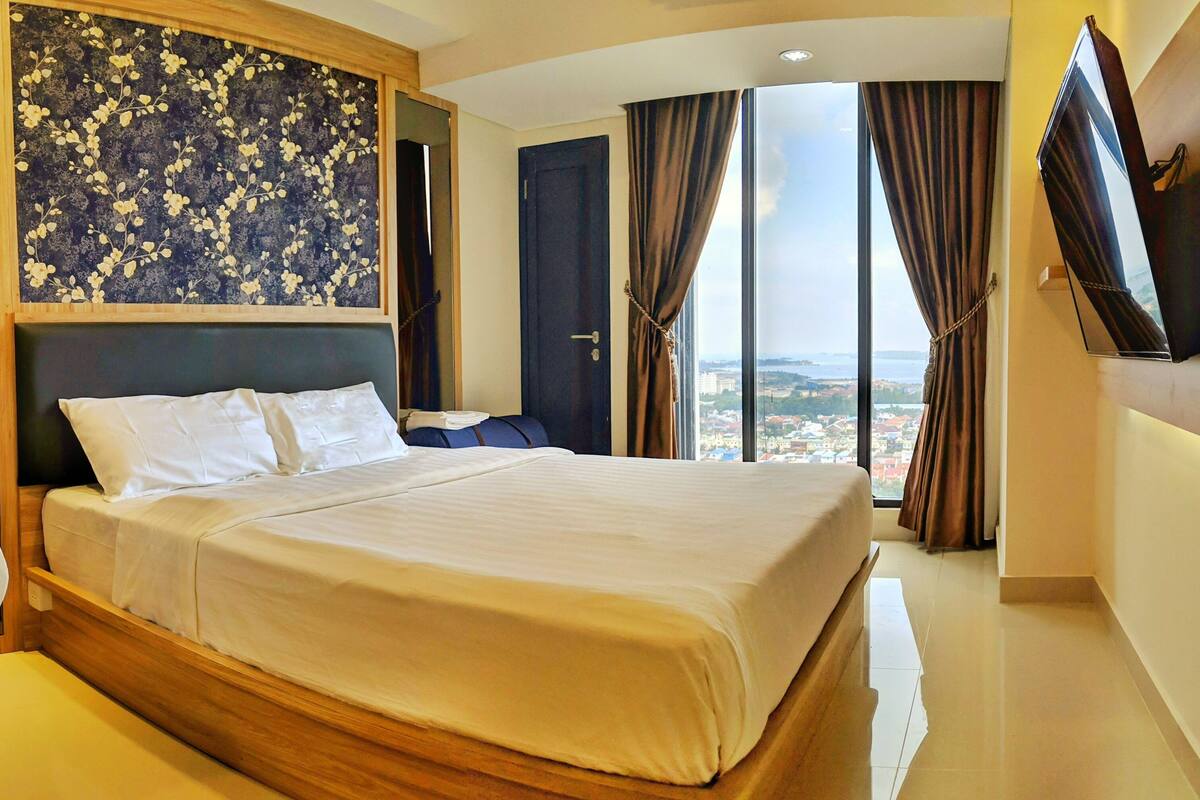 Une chambre d’hôtel avec un grand lit, une vue sur la ville et un téléviseur fixé au mur.