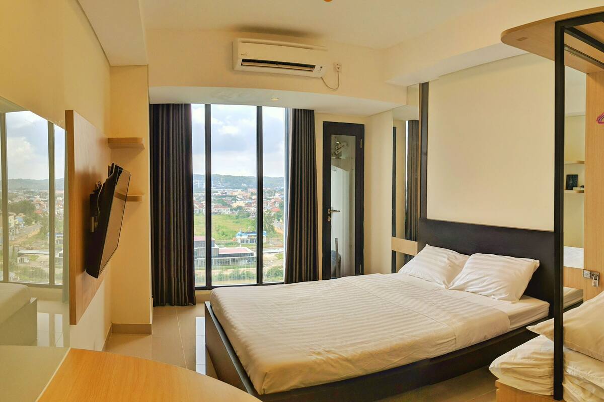 Une chambre d’hôtel moderne, dotée d’un grand lit, d’un bureau et offrant une vue sur le paysage urbain grâce à de grandes fenêtres.