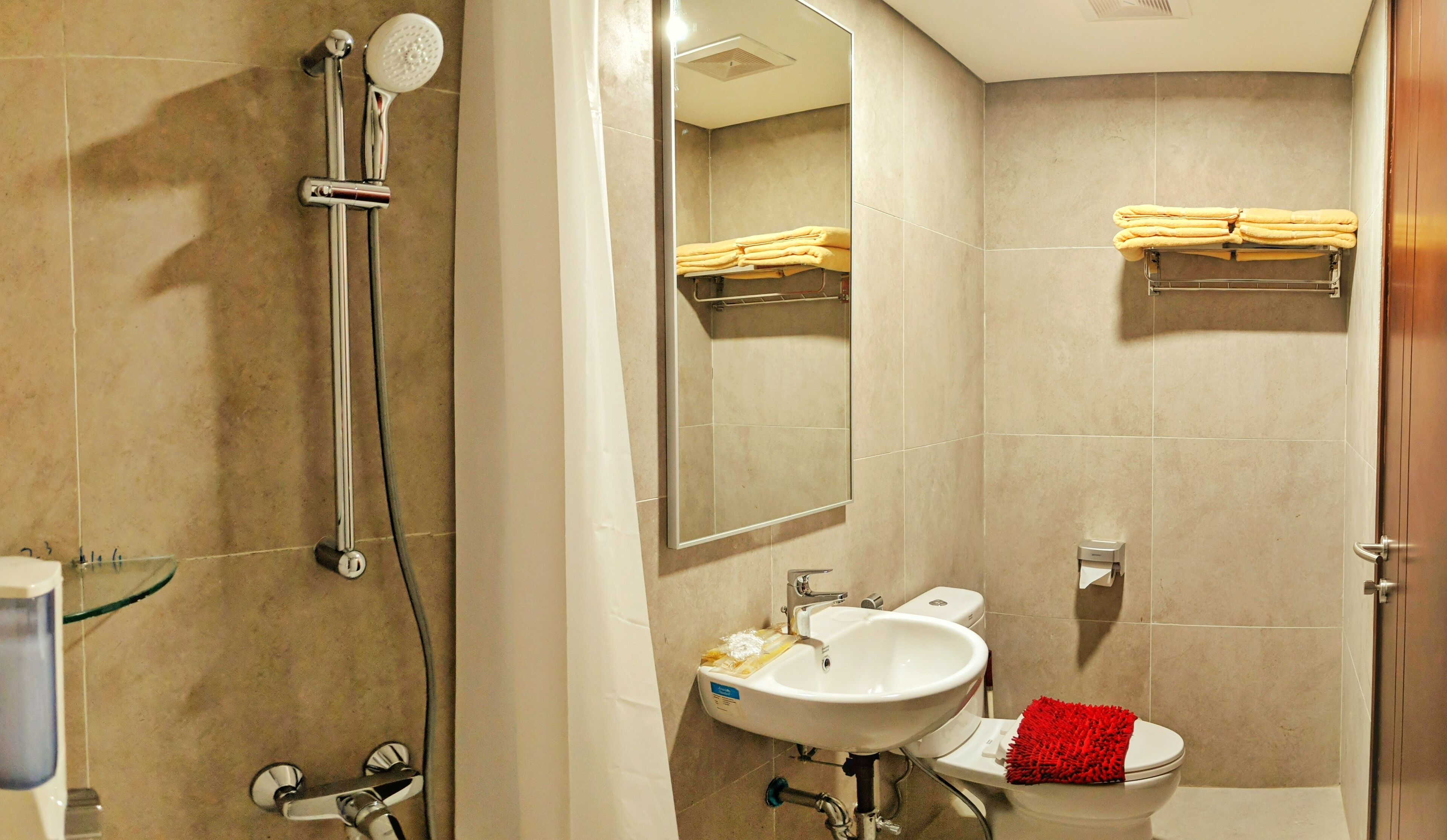 Un baño con ducha, lavamanos, inodoro y perchero para toallas.