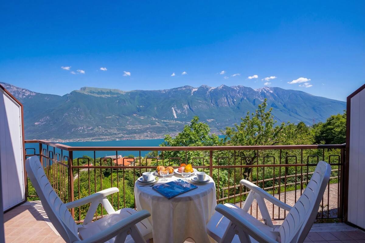 A balcony with a table set for breakfast, overlooking a mountainous landscape and a body of water.