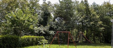A park with a swing set and a slide, surrounded by trees and grass.