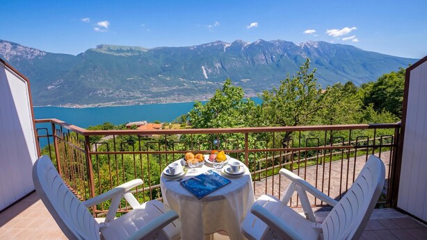 A balcony with a table set for two, overlooking a mountainous landscape and a body of water. - Appartamenti Secrel (Tremosine)