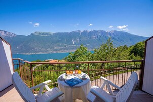 A balcony with a table set for two, overlooking a mountainous landscape and a body of water.