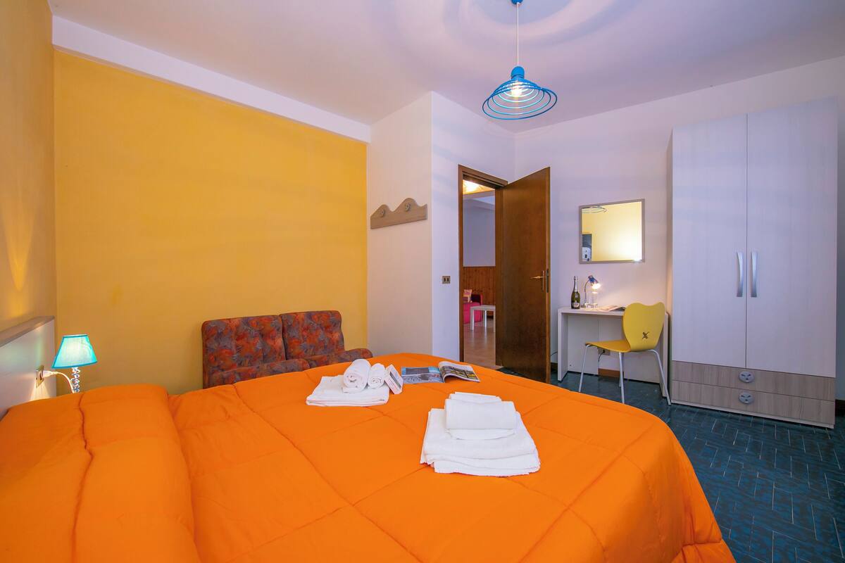 A hotel room with a bed, a desk, a chair, a wardrobe, and a mirror.