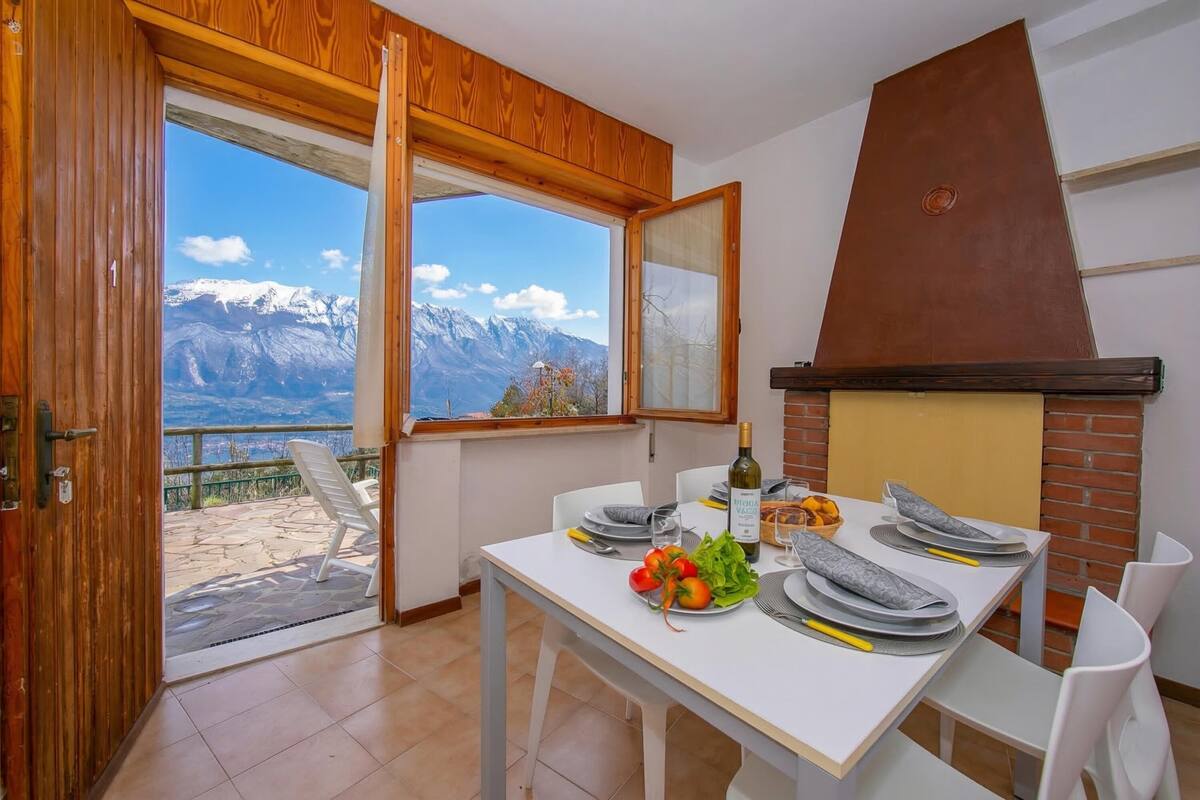 A dining area with a table set for two, a view of mountains, and a brick fireplace.