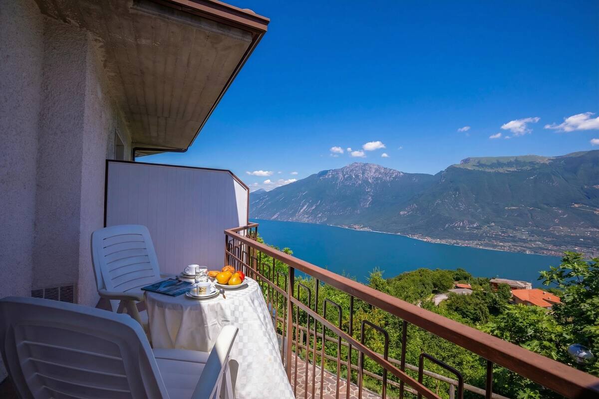 A balcony with a table set for two, overlooking a mountainous landscape and a body of water.
