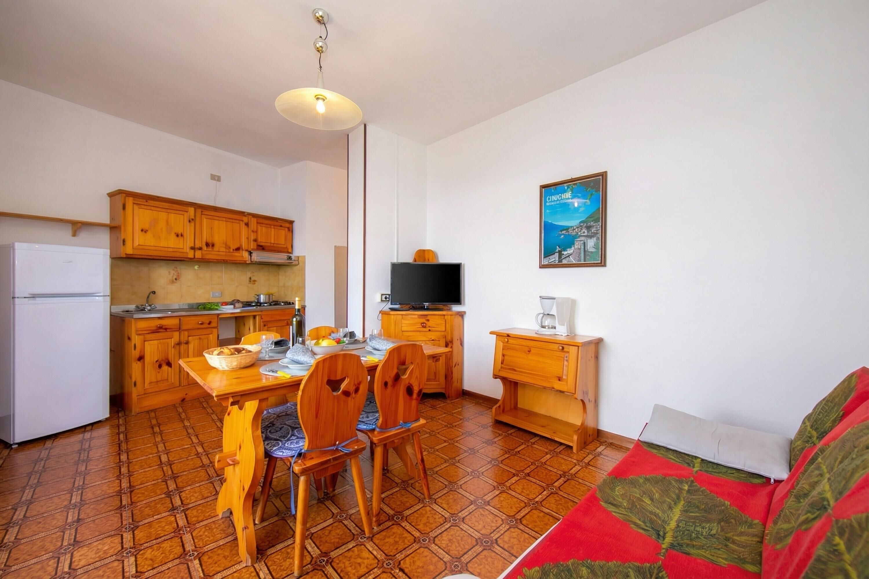 Une cuisine compacte avec des meubles en bois, une table à manger avec des chaises, un téléviseur et un tableau accroché au mur.