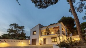 Una casa de dos pisos con entrada iluminada, balcón y camino de acceso pavimentado.