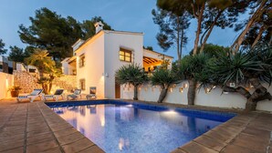 Una villa moderna con piscina, muros de piedra y un patio con sillones de descanso.