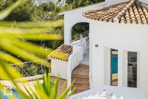 A white building with a tiled roof, a pool, and a view of greenery.