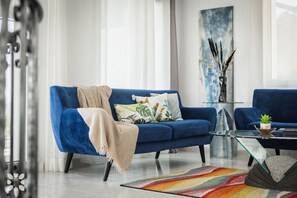 Uma sala de estar moderna com um sofá azul, uma mesa de centro de vidro e um tapete colorido.