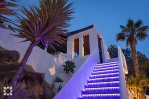 A building with a white exterior, a staircase with purple lighting, and palm trees.