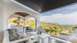 A modern outdoor seating area with white furniture, a table, and a view of a mountainous landscape. - Villa INFINIDAD by Abahana Villas (Moraira)